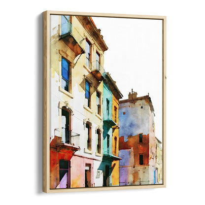Framed canvas print of a watercolor painting showing colorful buildings with pastel facades, set in a natural wood frame.