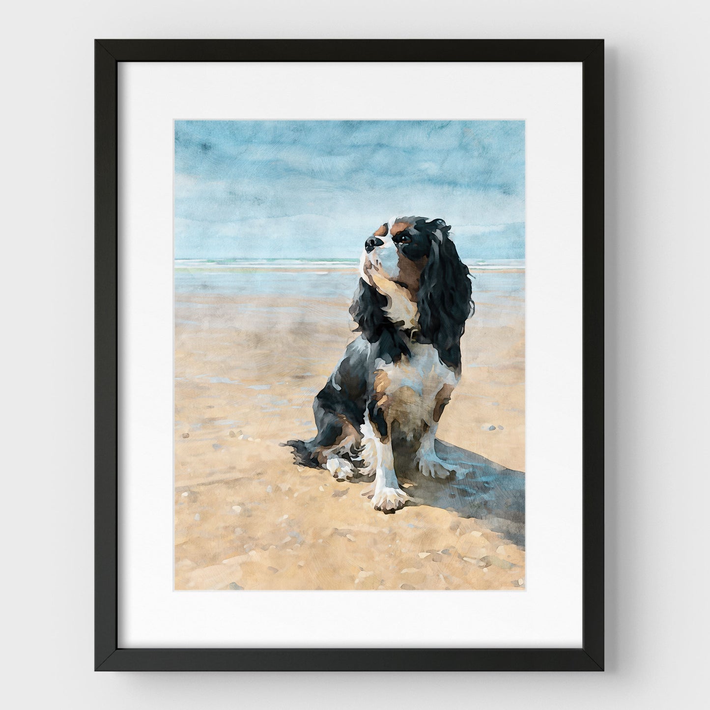 Black framed artwork with a white mat of a tricolor King Charles spaniel on a beach with a watercolor background