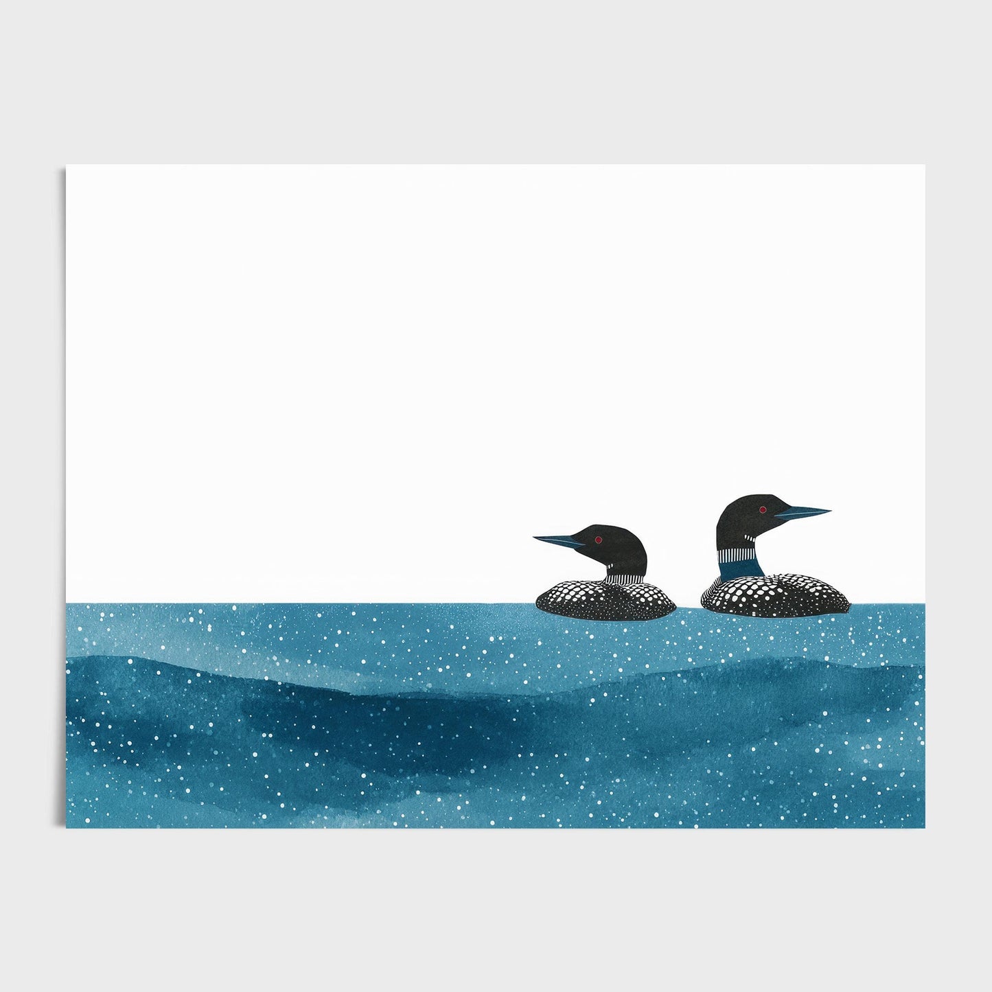 Minimalist art print featuring two common loons with black-and-white patterned plumage and red eyes, floating side by side in textured deep blue water speckled with white dots. The background is clean and white, creating a modern, airy contrast to the rich tones of the birds and water.