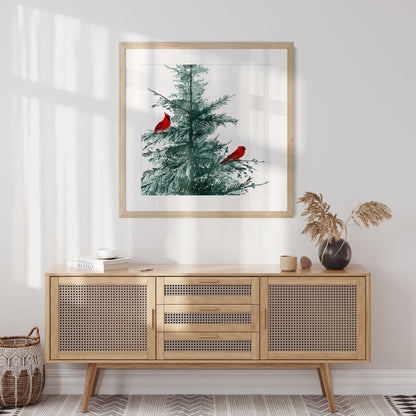 Framed watercolor art print of a pine tree with two bright red cardinals, hanging above a mid-century rattan sideboard in a light-filled modern room with neutral tones and minimalist decor.